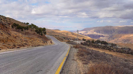 Road in mountainous terrain near At Tafilah, Jordan, Dead Sea at distant background
