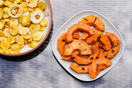 Grilled potatoes and orange butternut squash pieces on two plates - top down viewの写真素材