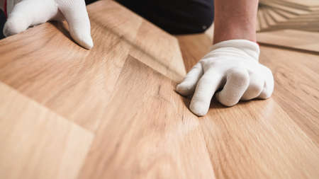 Installing laminated floor, detail on man hands in white gloves fitting wooden tilesの写真素材