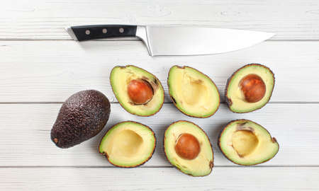Avocado - Hass / Bilse variety - halves arranged on white boards desk, some of them over ripen,...