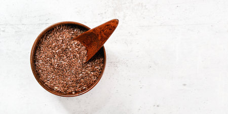 Small wooden bowl full of common flax linseed - Linum usitatissimum - little scoop inside, on white...