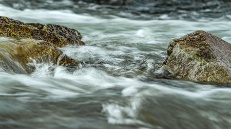 Rapid spring river flowing over rocks forming white water waves, closeup detail - abstract nature backgroundの写真素材