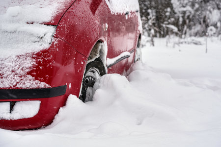 Red car parked in deep layer of snow after heavy snowstorm, detail to tire - only half wheel visibleの写真素材