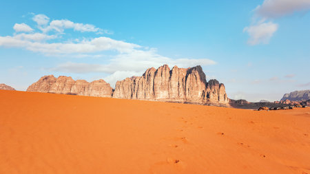 Orange sand desert, rocky formations and mountains background, blue sky above, camp tents visible at distance - typical scenery in Wadi Rum, Jordanの写真素材