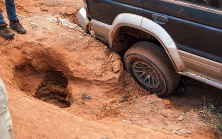 4wd vehicle driving over road with extreme holes and bumps, close up on rear wheel - roads are in...