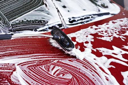 Red car washed in self serve carwash, detail to brush leaving strokes on hood in white foamの写真素材
