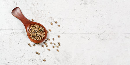 Unpeeled hemp - Cannabis sativa - in small dark wooden spoon on white stone board desk, space for text right sideの写真素材