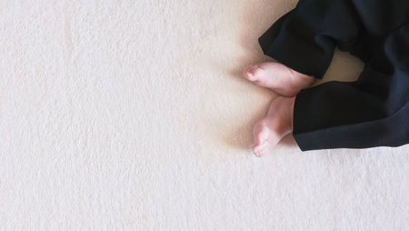Baby boy legs in black trousers, on white towel cloth, view from above, wide banner with space for...