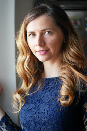 Natural light portrait of young woman with long waves hair, wearing dark blue dress, blurred steel...