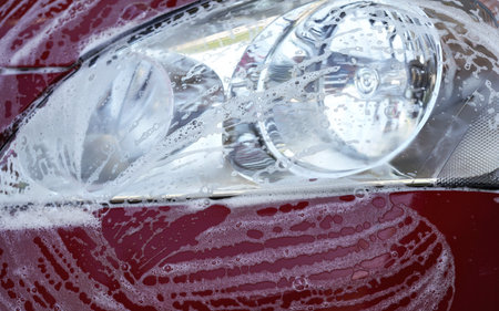 Front light of red car washed in carwash detail on soap foam with strokes over glassの写真素材