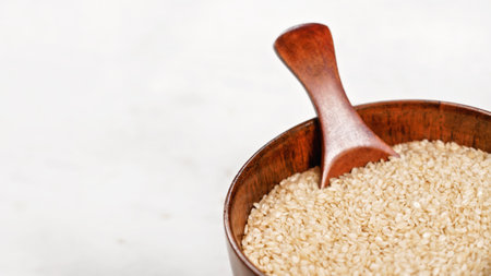 White sesame - Sesamum indicum - seeds in small wooden cup with spoon on white board, space for text left sideの写真素材