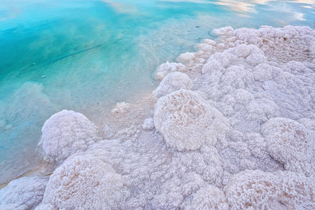 Sand completely covered with crystalline salt on shore of Dead Sea, turquoise blue water near -...