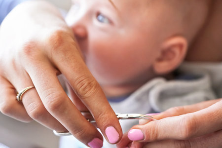 Infant baby boy having his nails cut by mother, detail on scissors and fingertips