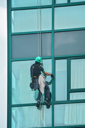 Industrial window cleaner - man hanging on roofs with safety equipment, cleaning facade of tall...