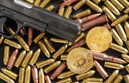 Bronze and brass gun bullets scattered on dark table, black pistol barrel, golden bitcoin coins near - illegal use of cryptocurrency to purchase weapon conceptの写真素材