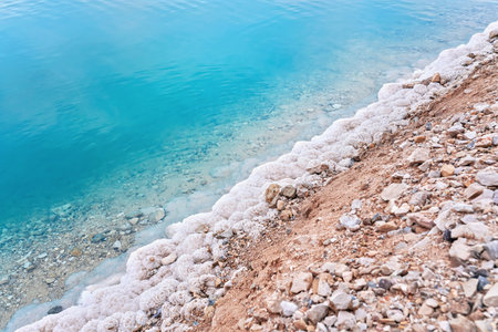 Sand covered with crystalline salt on shore of Dead Sea, turquoise blue water near - typical scenery at Ein Bokek beach, Israelの写真素材