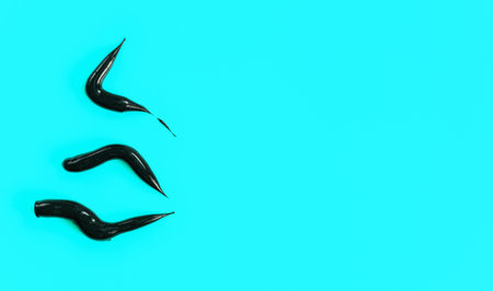 Three thick black cream smears (charcoal toothpaste) on light blue background, view from above,...