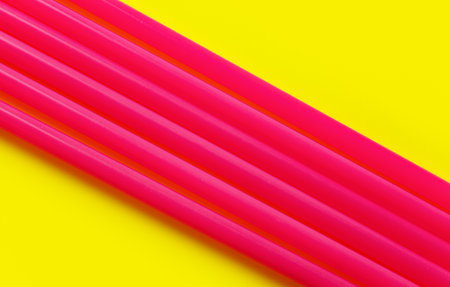 Six pink plastic drinking straws on yellow board, forming diagonal line - abstract closeup detailの写真素材