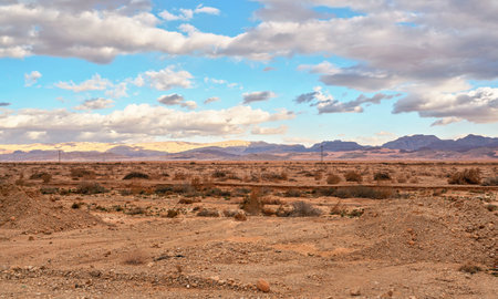 Typical landscape at Israel Jordan border. Flat dry desert with low bushes and small mountains, sun shines through evening cloudsの写真素材