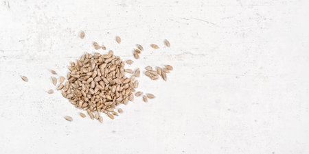 Small pile of peeled sunflower seeds on white stone board, closeup view from above, empty space...