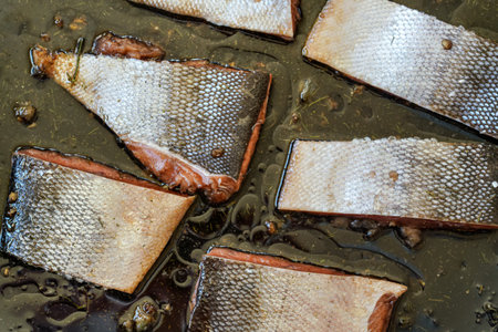 Pieces of salmon with skin in cooking oil and some herbs on frying pan - to be baked