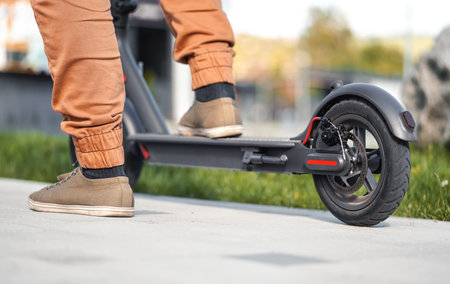 Man feet on electric scooter, closeup detail, sun lit blurred grass in backgroundの写真素材
