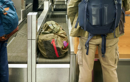 Passenger standing next to checked in bags and luggage on transport belt of airport check-in desk, view from behindの写真素材