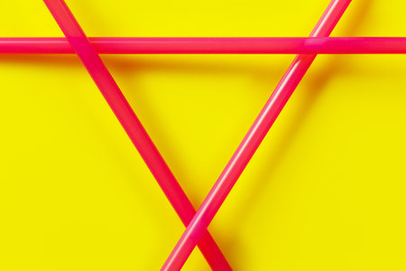 Three pink plastic drinking straws arranged in triangle, closeup detail over yellow backgroundの写真素材