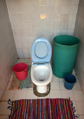 Provisional porcelain toilet without flushing mechanism installed in room without pipes or plumbing, green barrel with water nearの写真素材