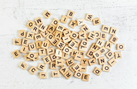 Pile of wooden tiles with various letters scattered on white stone like board, view from aboveの写真素材