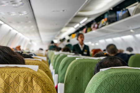 Commercial plane interior before take off, focus on man head at seat ahead, most of passengers already seated, baggage compartments still opened, blurred stewardess in backgroundの写真素材