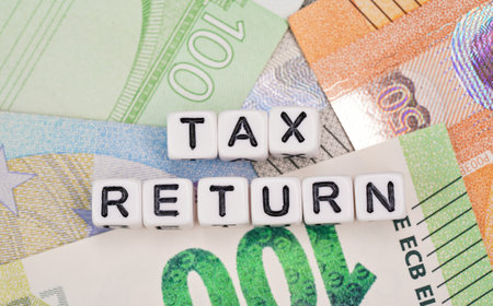 Small white beads with black letters TAX RETURN on euro banknotes, closeup detail from aboveの写真素材