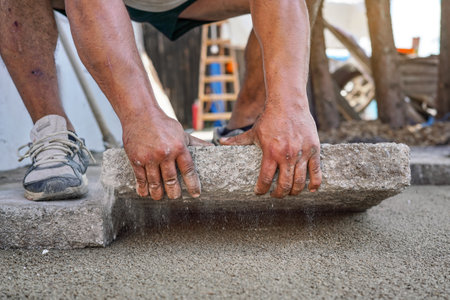Installing new pavement or floor outside from large concrete tiles, closeup detail on male worker fitting stone block over sand and gravel base layerの写真素材