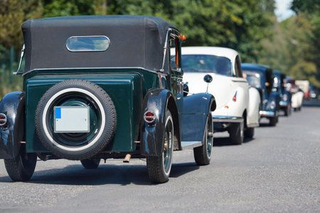 Row of old vintage cars driving down the road on sunny day, view form behindの写真素材