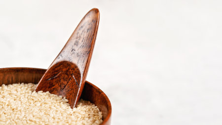 White sesame - Sesamum indicum - seeds in small wooden bowl with scoop closeup detail, space for text right sideの写真素材