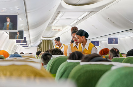 Addis Ababa, Ethiopia - April 23, 2019: Commercial plane interior during flight, passengers seated, baggage compartments closed, African female attendant serving drink and foodのeditorial素材