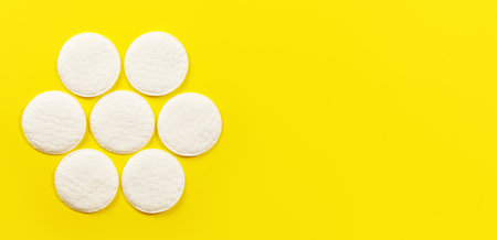 Top down view, 7 face cleaning cotton pads arranged in circle, on yellow board, wide banner space for text rightの写真素材