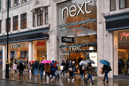 London, United Kingdom - February 01, 2019: People walk at NEXT department store at their central London branch on a rainy day, blurred main road with red buses backgroundのeditorial素材