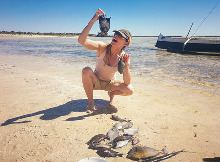 Young woman in shorts and t shirt posing with freshly caught sea fish, holding it near mouthの写真素材