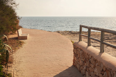 Stone road with wooden fence by sea cliff lit by morning sunの写真素材