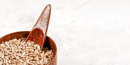 Peeled sunflower seeds in small wooden bowl or cup with spoon on white board, space for text right sideの写真素材