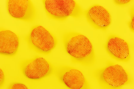 Potato crisps orange from paprika flavouring arranged on yellow board, view from above