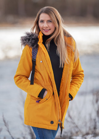 Casual portrait of young woman in warm orange yellow winter jacked, zipper down, smiling, blurred background behind herの写真素材
