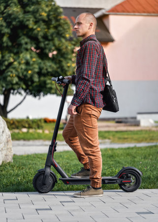 Young man in casual trousers and shirt standing next to his electric scooterの写真素材