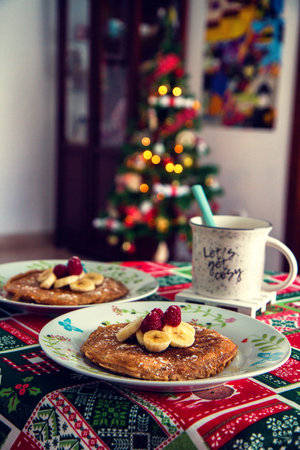 Homemade pancakes topped with banana and strawberries with a hot cocoa on the side and Christmas...