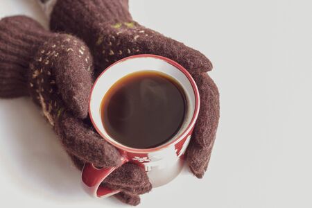 hands in brown gloves with a New Year pattern hold a red cup with hot coffee on a white background. Top view Flat lay Winter evening Card.の写真素材