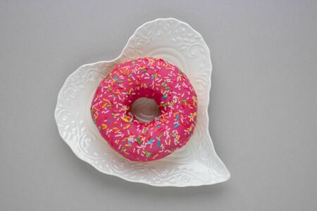 Donut with colorful sprinkles isolated lying on a white plate on gray background. Top view.の写真素材