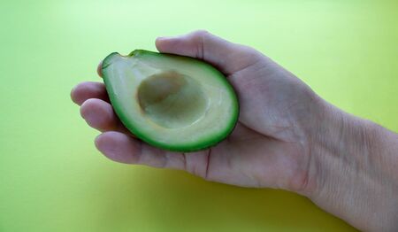 Half avocado with bone in hand on yellow background.の写真素材