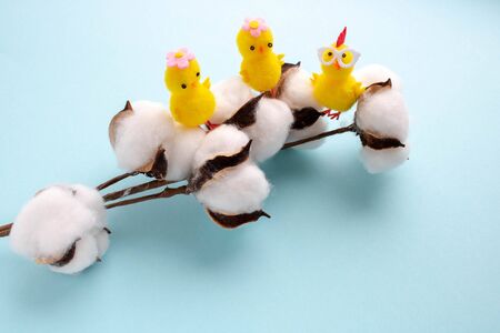 Small toy yellow chickens sit on a branch of white cotton