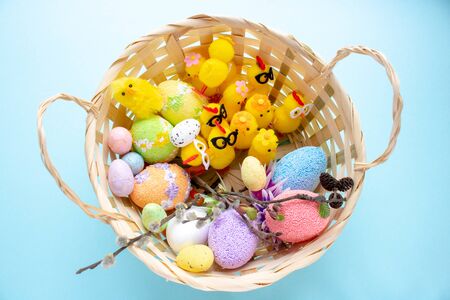 In the Easter basket sit yellow toy chickens and lay colorful eggs on a blue background